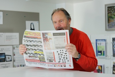 Heikki Orama kirjastossa. Hassu kuva, jossa hän pitää lehti väärinpäin.